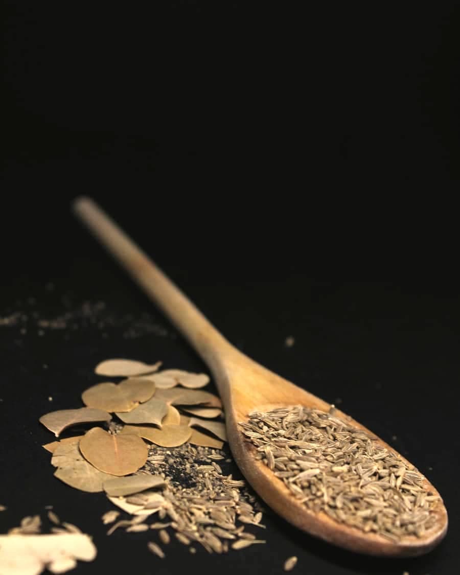 Cumin seeds on a wooden spoon with bay leaves