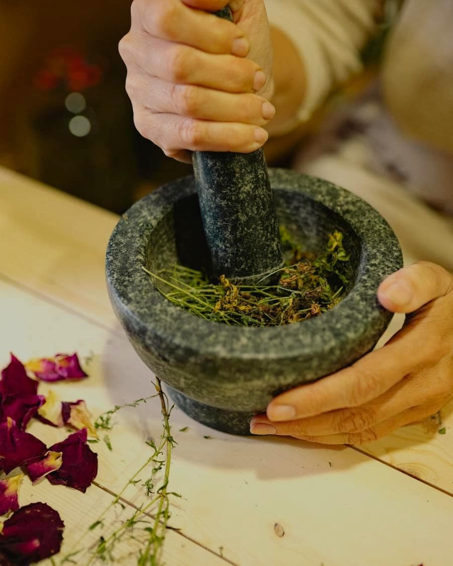 Hands grinding spices in a stone mortar on a pale wooden table