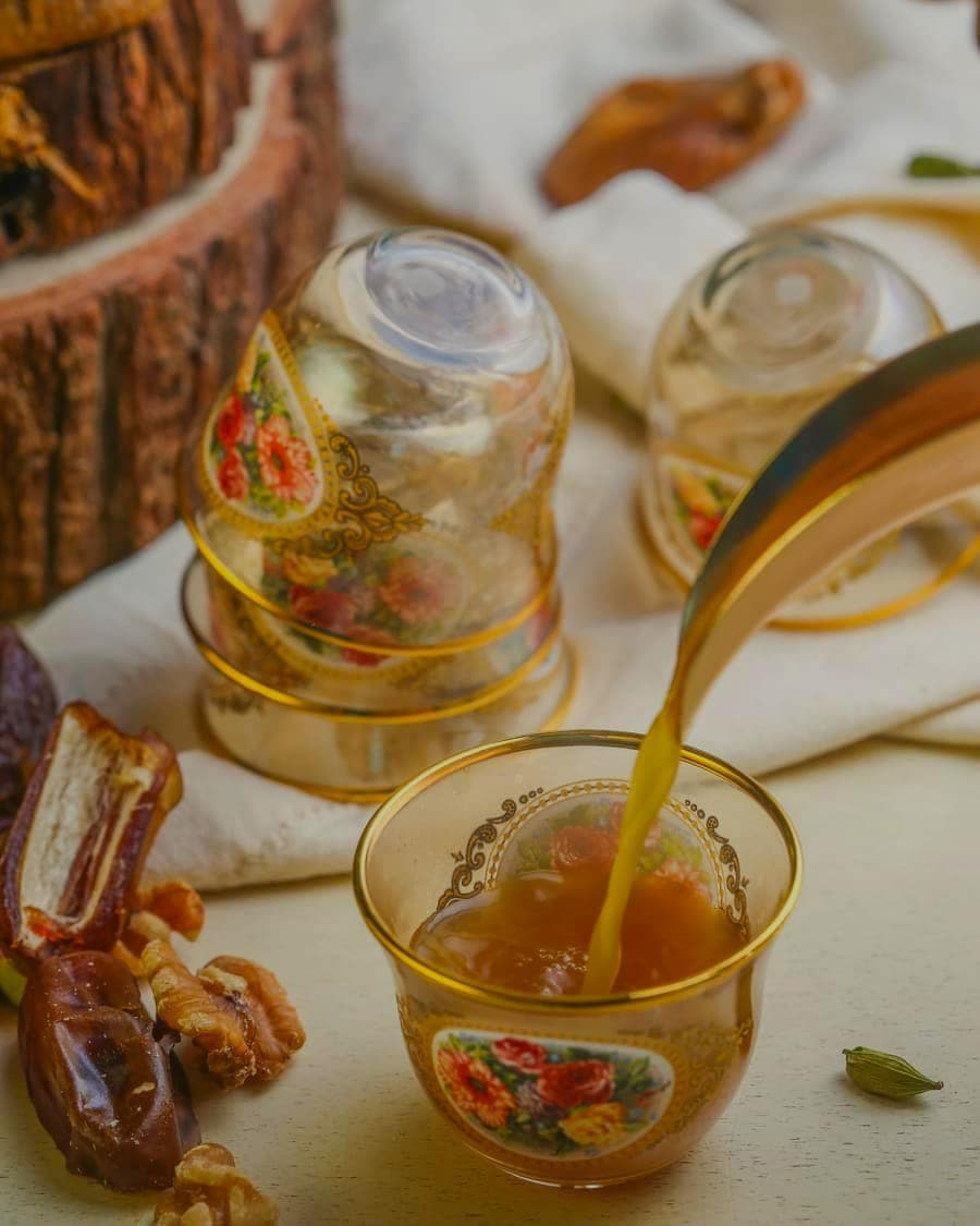 Spiced tea poured into a small ornate glass beside dates and nuts