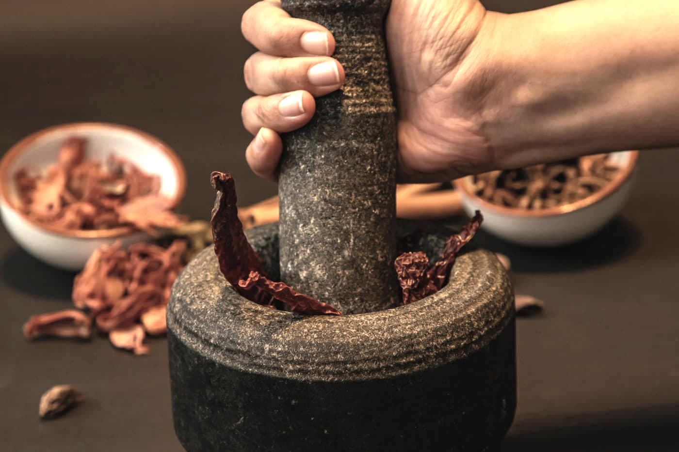 A hand crushing dried chillies with a stone pestle