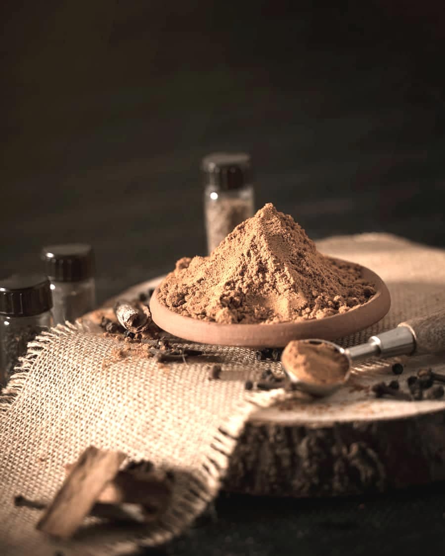 A mound of red-brown ground spice blend on a wooden plate with sacking behind