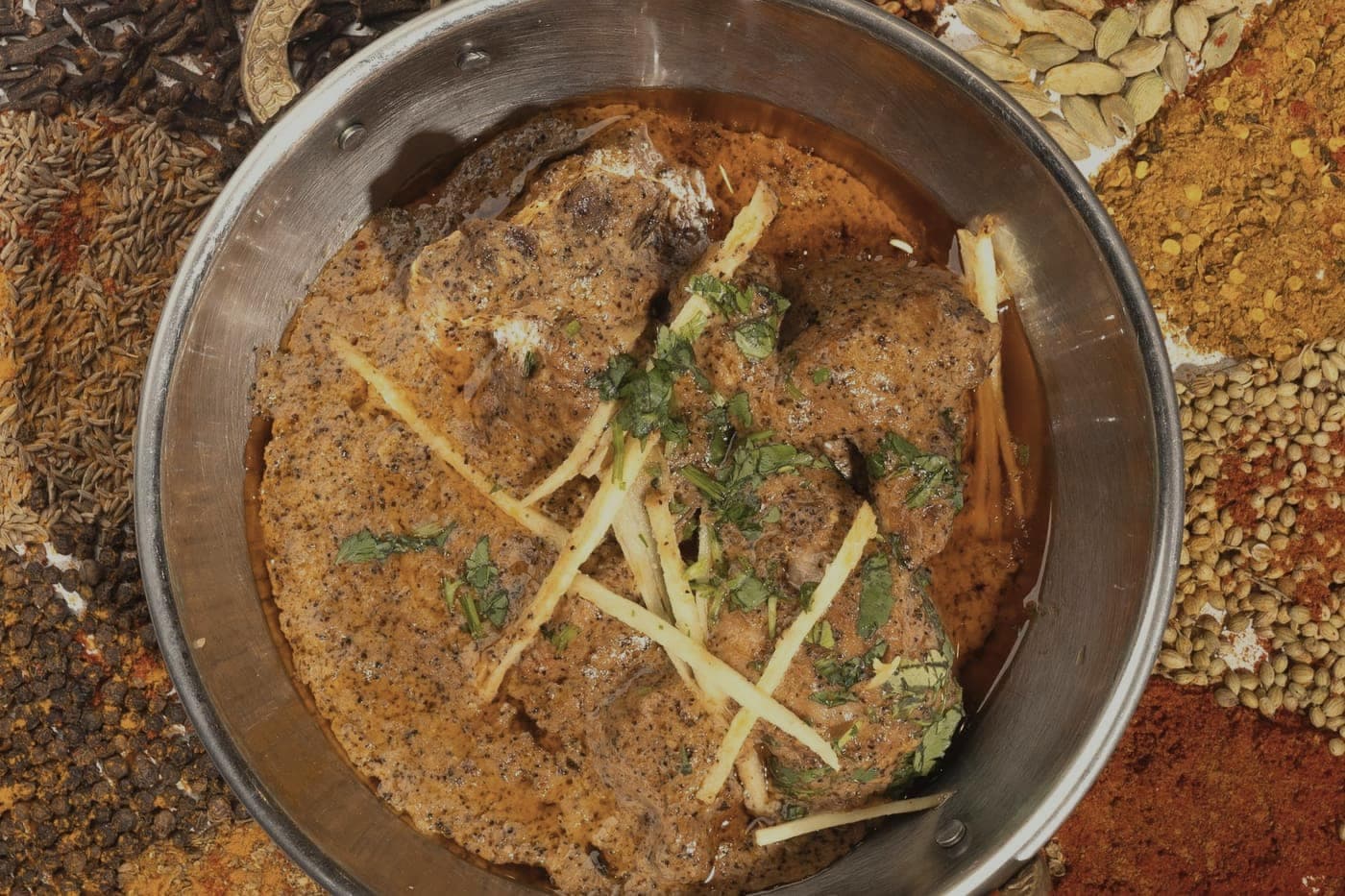 Rogan josh in a steel dish surrounded by ground spices