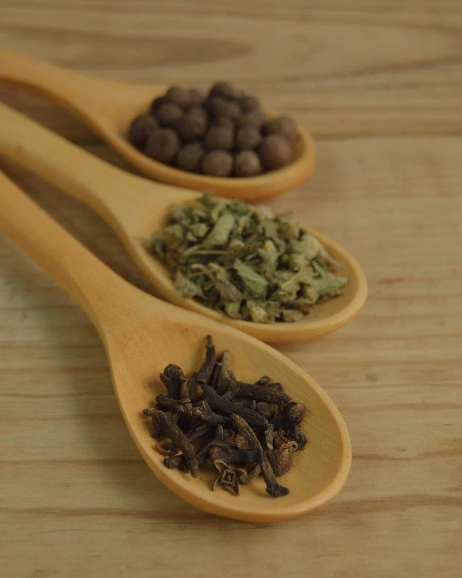 Wooden spoons holding cloves, herbs and peppercorns on a warm table