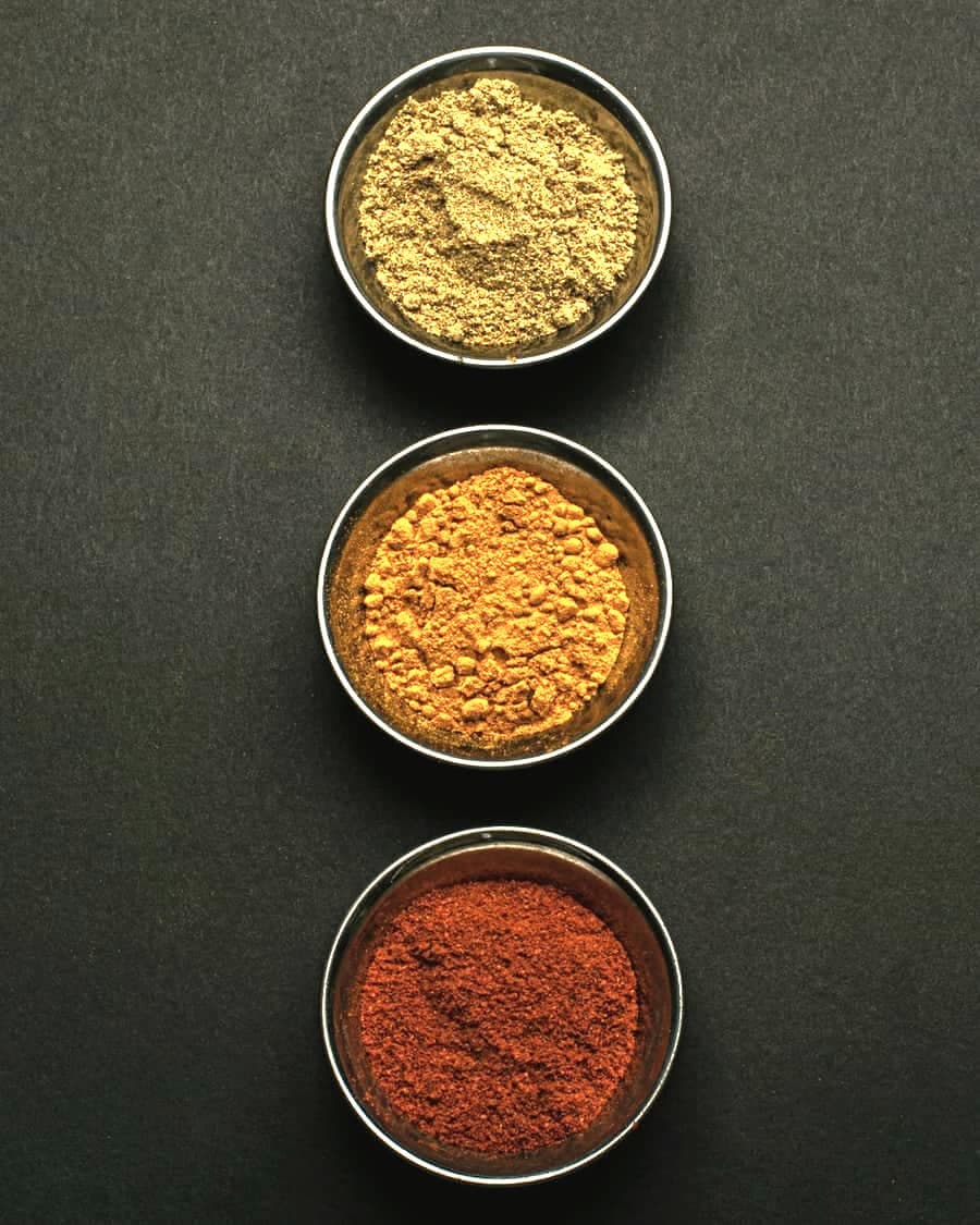 Three small metal bowls of ground spice on a dark ground