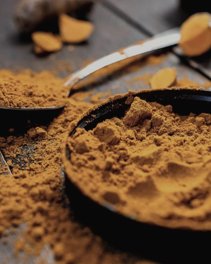 Ground turmeric heaped in a dark bowl on a wooden surface