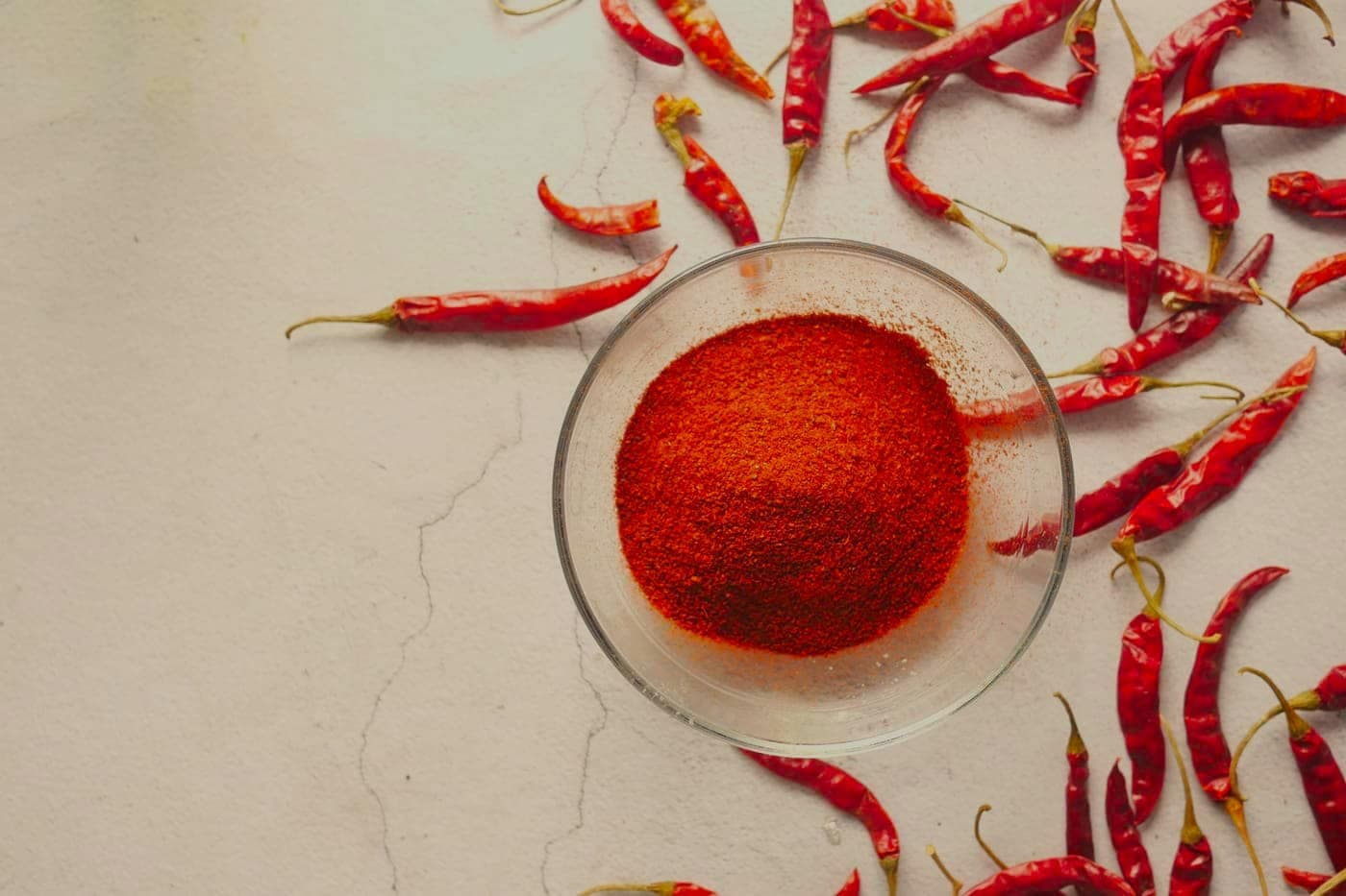 Ground chilli in a glass bowl with whole chillies scattered around it